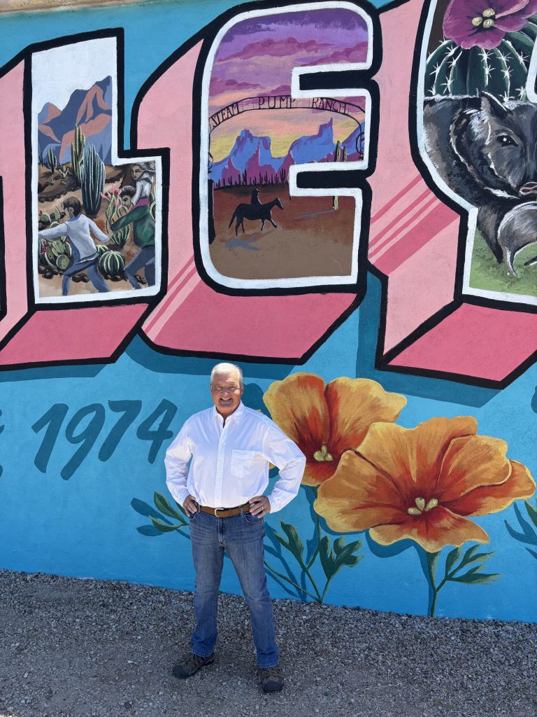 OVHS President, Bob Kellar, stands in front of the Welcome to Oro Valley Mural at Oro Valley Marketplace by local artist, Pen Macias.